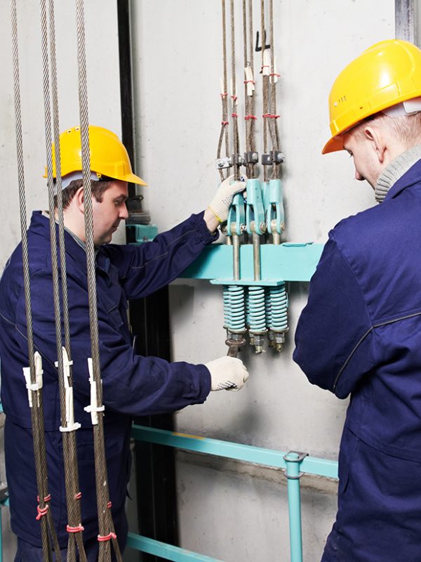 two machinist worker technicians at work adjusting lift with spanners in elevator hoistway